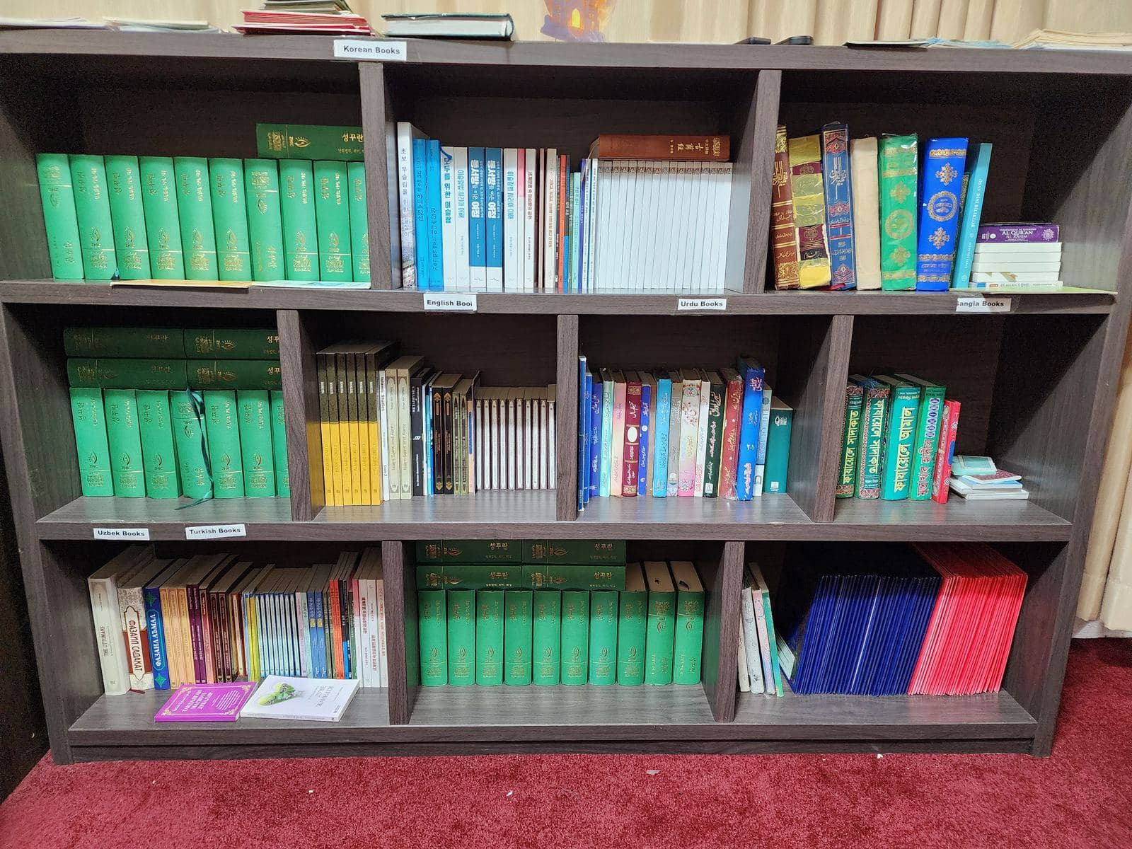 Library shelves with labeled sections — Korean, English, Urdu, Bangla, Uzbek, and Turkish books